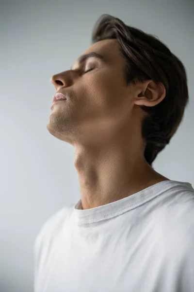 Retrato de hombre morena con los ojos cerrados posando aislado sobre gris - foto de stock