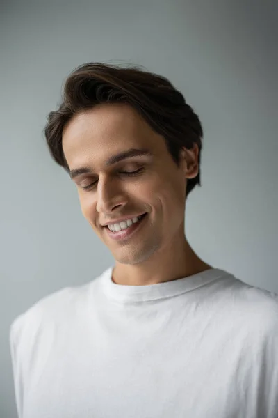 Retrato de hombre feliz en camiseta blanca sonriendo aislado en gris - foto de stock