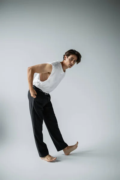 Full length of stylish man in white t-shirt and black pants posing with hand in pocket on grey — Stock Photo