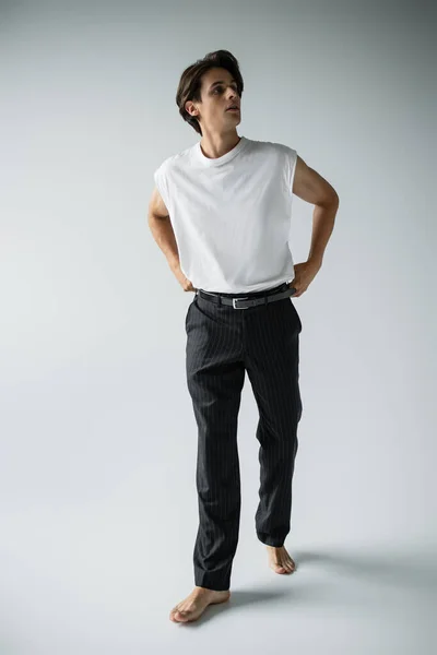 Homme pieds nus en t-shirt blanc et pantalon noir posant debout sur gris — Photo de stock