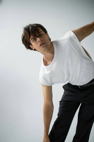 Stilvoller Mann in weißem T-Shirt und schwarzer Hose blickt in die Kamera auf grau — Stockfoto