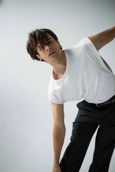 Homme élégant en t-shirt blanc et pantalon noir regardant caméra sur gris — Photo de stock