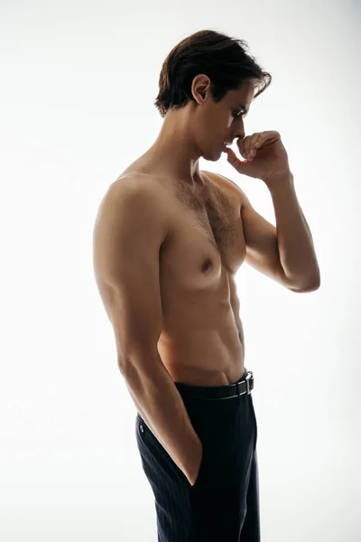 Visão lateral do homem muscular e sem camisa em calças pretas posando com a mão no bolso no branco — Fotografia de Stock