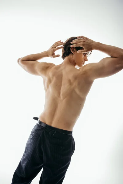 Vista lateral del hombre musculoso y sin camisa en pantalones negros mirando hacia otro lado en blanco - foto de stock