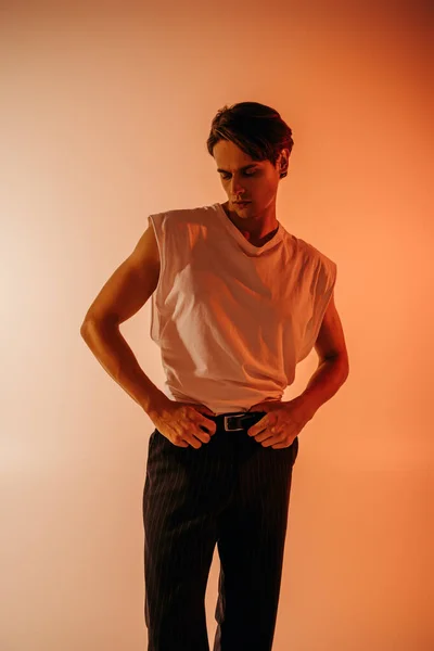 Hombre con estilo en camiseta blanca y pantalones negros posando en naranja con degradado - foto de stock