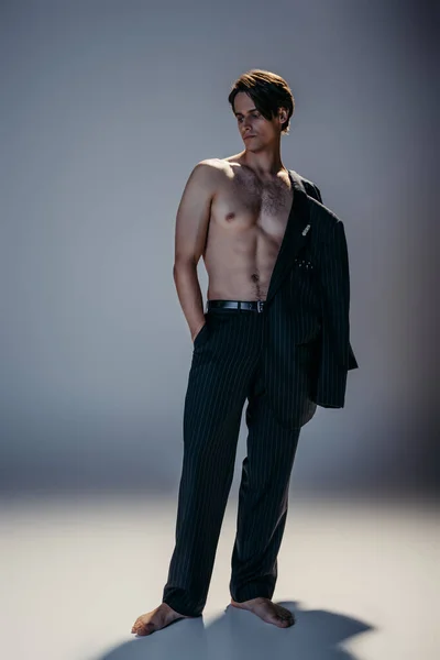 Volle Länge des muskulösen Mannes mit behaarter Brust und stilvollem Anzug posiert mit der Hand in der Tasche auf dunkelgrau — Stockfoto