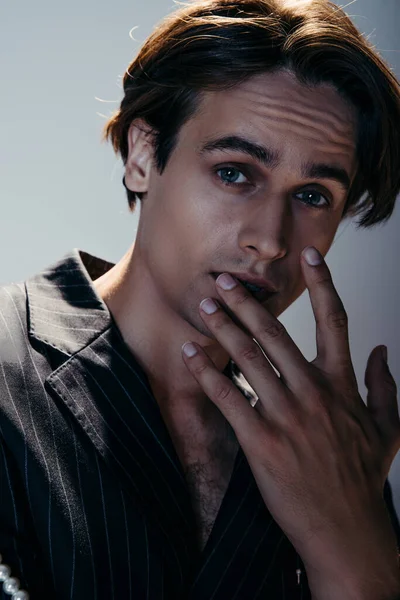 Hombre con estilo en traje de moda labio endurecido mientras posa aislado en gris - foto de stock