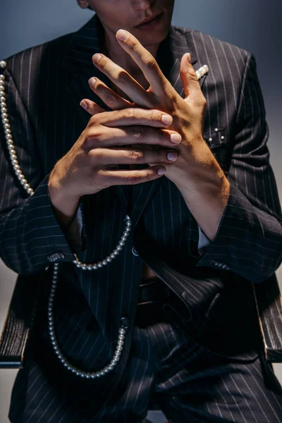 Vista recortada de hombre con estilo en traje de moda con cadena de perlas gestos en gris oscuro - foto de stock