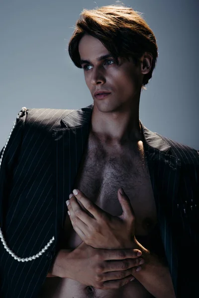 Stylischer Mann im trendigen Anzug mit Perlenkette schaut weg auf dunkelgrau — Stockfoto