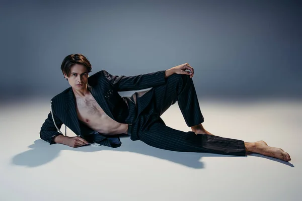 Elegante hombre de traje con perlas y pecho peludo posando sobre fondo gris oscuro - foto de stock