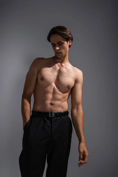 Gut aussehender Mann mit muskulösem Körper posiert mit der Hand in der Tasche einer schwarzen Hose auf grau — Stockfoto