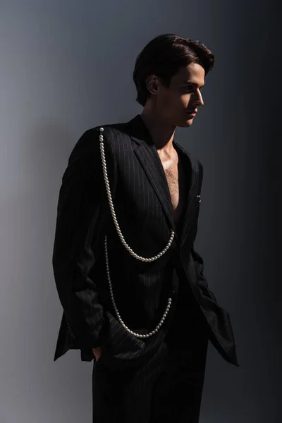 Man in trendy suit with pearls looking away while posing with hands in pockets on dark grey — Stock Photo