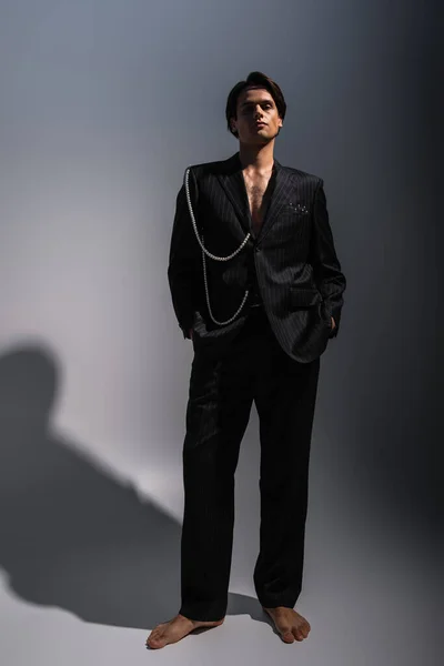 Full length of barefoot man in trendy suit with pearls posing with hands in pockets on dark grey — Stock Photo