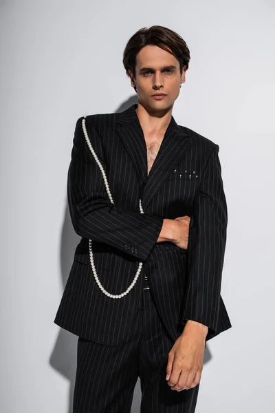 Brünetter Mann im trendigen Anzug mit Perlen posiert vor der Kamera auf grau — Stockfoto