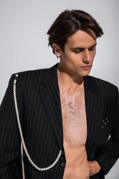 Brunette man in trendy jacket with pearls posing while looking away isolated on grey — Stock Photo