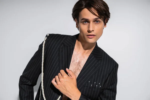 Brunette man in trendy jacket with pearls posing while looking at camera isolated on grey — Stock Photo