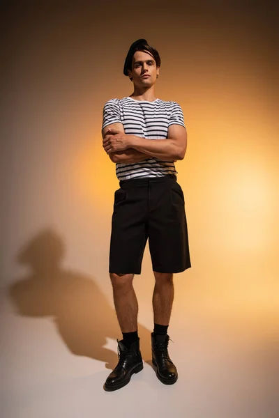Full length of man in beret and striped t-shirt standing with crossed arms on orange — Stock Photo