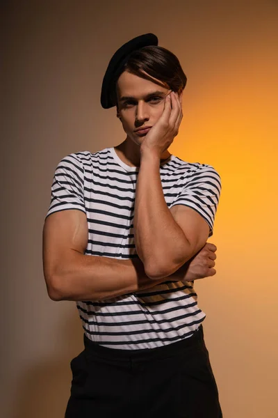 Stylish man in beret and striped t-shirt looking at camera while posing on orange — Stock Photo