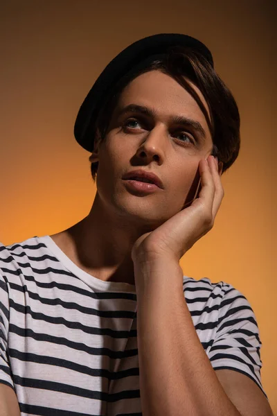 Portrait of dreamy man in beret and striped t-shirt looking away while posing on orange — Stock Photo