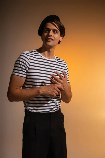 Stylish man in beret and striped t-shirt looking away while smiling on orange — Stock Photo