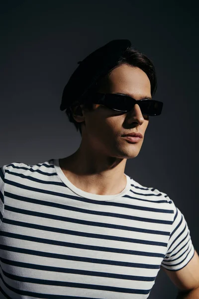 Portrait of brunette man in sunglasses and striped t-shirt isolated on grey with lighting — Stock Photo