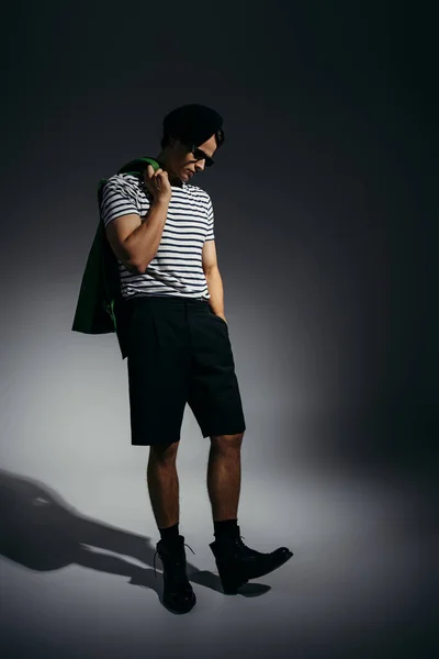 Brünetter Mann in Sonnenbrille und gestreiftem T-Shirt mit Lederjacke auf grauem Hintergrund mit Schatten — Stockfoto