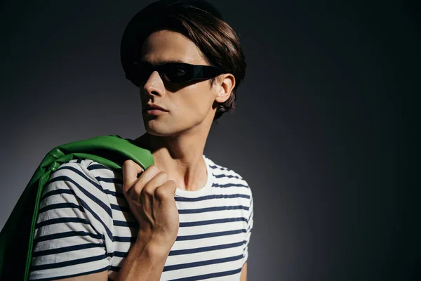 Stylish man in sunglasses holding green leather jacket isolated on grey with lighting — Stock Photo