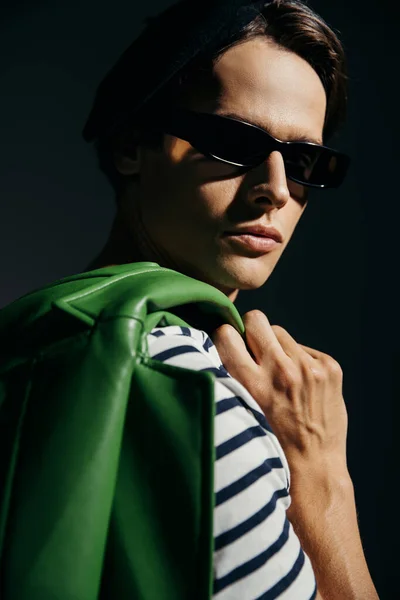 Портрет брюнетки в сонцезахисних окулярах, що тримає розмиту шкіряну куртку ізольовано на сірому з освітленням — стокове фото