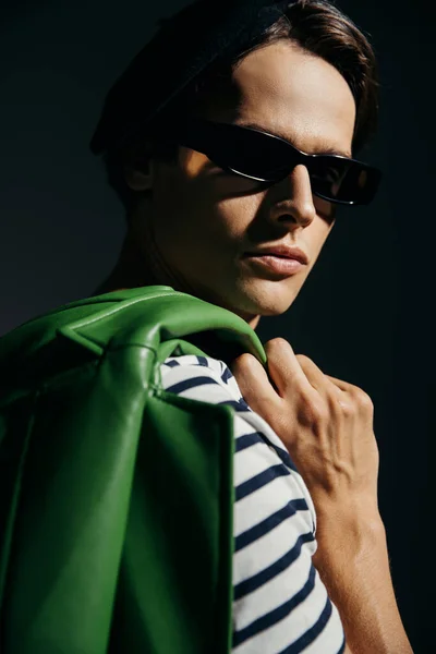 Retrato de hombre morena en gafas de sol sosteniendo chaqueta de cuero borrosa aislado en gris con iluminación - foto de stock