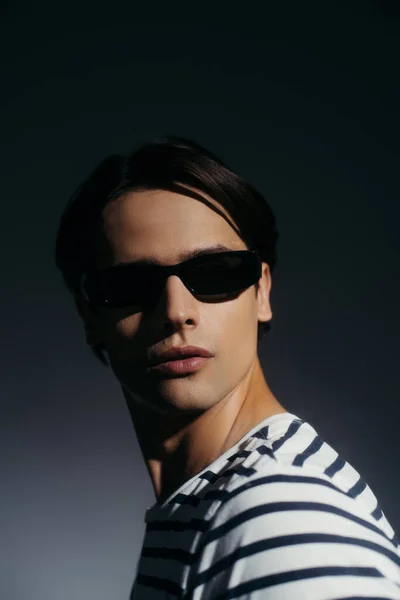 Brunette model in sunglasses posing on grey background with lighting — Stock Photo