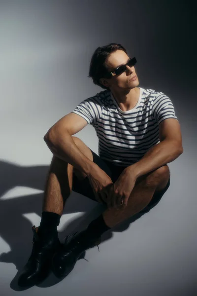 Modelo elegante em óculos de sol e sapatos posando em fundo cinza com sombra — Fotografia de Stock