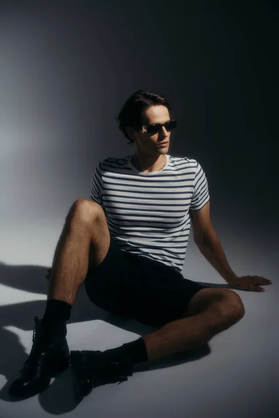 Homme élégant en lunettes de soleil posant sur fond gris avec éclairage — Photo de stock