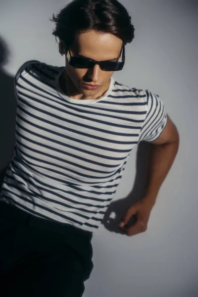 High angle view of model in striped t-shirt and sunglasses on grey background with lighting — Stock Photo