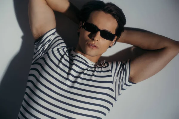 Draufsicht eines muskulösen Mannes mit Sonnenbrille und T-Shirt auf grauem Hintergrund mit Schatten — Stockfoto