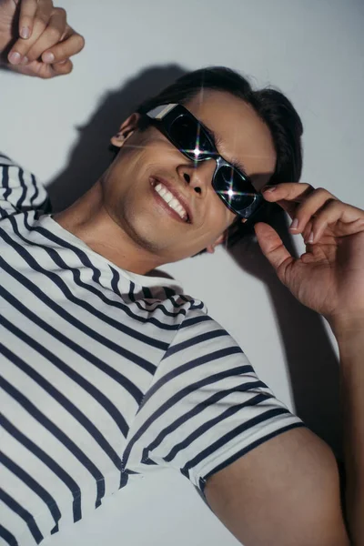 Vista de ángulo alto del hombre sonriente con gafas de sol brillantes sobre fondo gris con iluminación y sombra - foto de stock