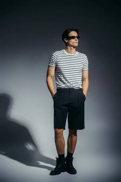 Comprimento total de homem elegante em shorts e botas em fundo cinza com sombra — Fotografia de Stock