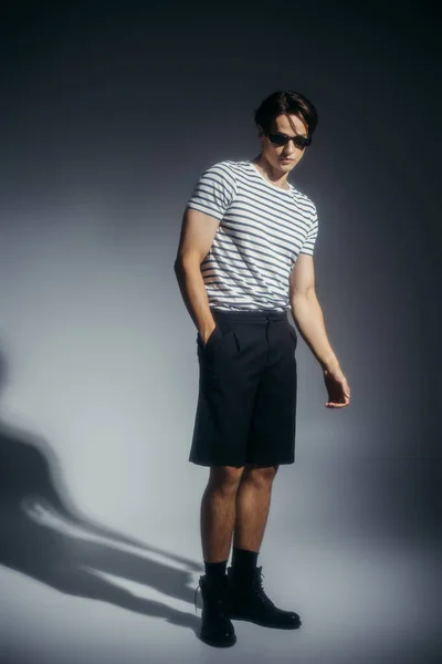 Modèle à la mode en lunettes de soleil et bottes sur fond gris avec ombre — Photo de stock