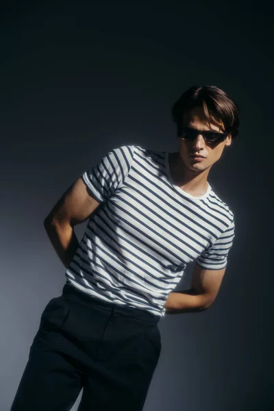 Élégant brunette homme aux lunettes de soleil posant sur fond gris — Photo de stock