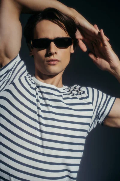 Hombre elegante y musculoso en gafas de sol posando aislado sobre gris con iluminación - foto de stock