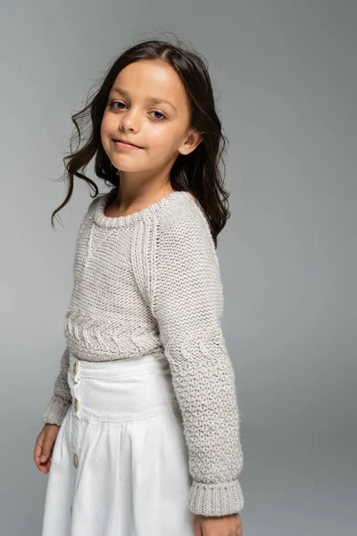 Smiling girl in warm sweater and white skirt looking at camera isolated on grey — Stock Photo