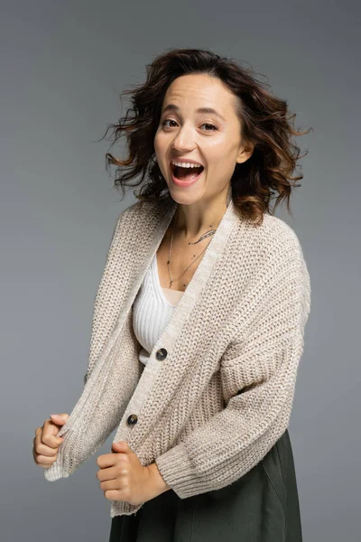 Excited woman in knitted cardigan laughing at camera isolated on grey — Stock Photo