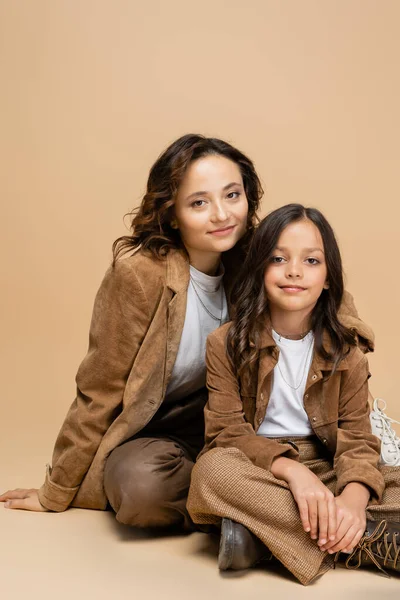 Femme et enfant en vestes et pantalons d'automne à la mode souriant à la caméra sur fond beige — Photo de stock