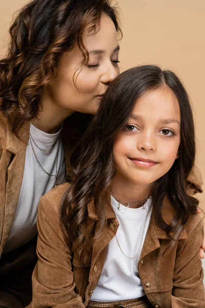 Mujer feliz con los ojos cerrados besando el pelo de la hija de moda sonriendo a la cámara aislada en beige - foto de stock