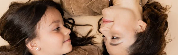 Top view of smiling mother and child looking at each other while lying on beige background, banner — Stock Photo