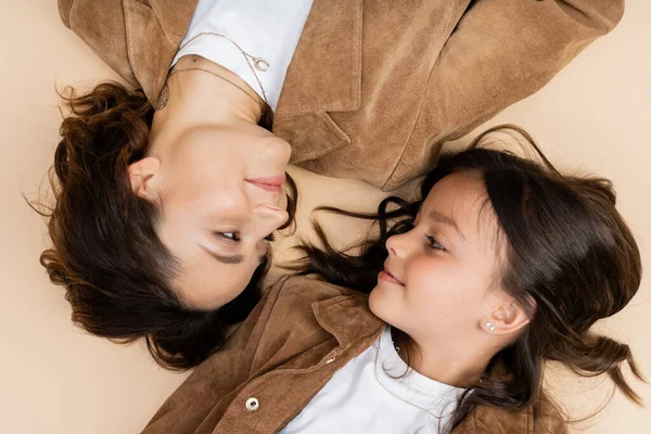 Top view of mom and daughter in trendy autumn jackets smiling at each other on beige background — Stock Photo