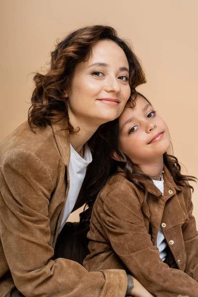 Brunette woman and girl in stylish autumn jackets smiling at camera isolated on beige — Stock Photo