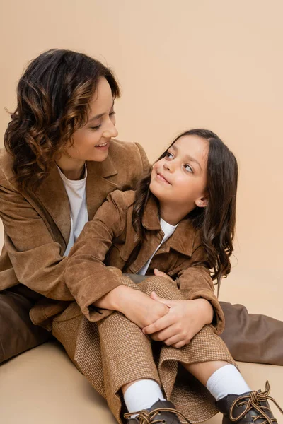 Joyeuse femme et enfant dans des vestes élégantes en daim regardant les uns les autres sur fond beige — Photo de stock