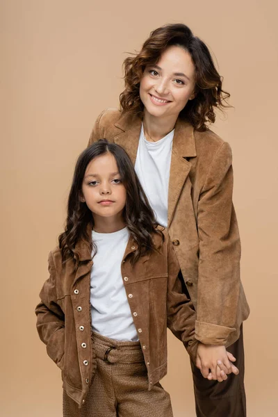 Fröhliche Frau hält Händchen mit angesagter Tochter, die isoliert auf Beige posiert — Stockfoto