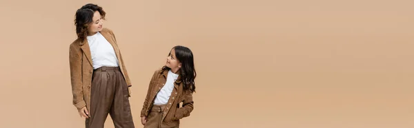 Mujer alegre y chica en ropa de otoño de moda mirándose aislados en beige, pancarta - foto de stock