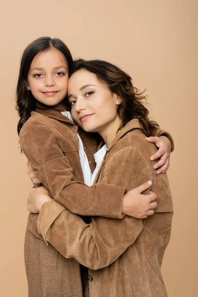 Jovem mulher e menina em casacos de outono elegantes abraçando e sorrindo para a câmera isolada no bege — Fotografia de Stock